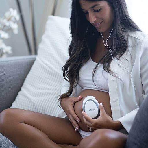 Woman holding a heart rate device against her pregnant belly.