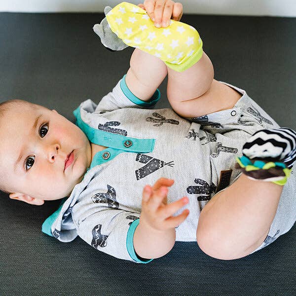 Baby lying on a dark surface holding yellow socks with white polka dots.