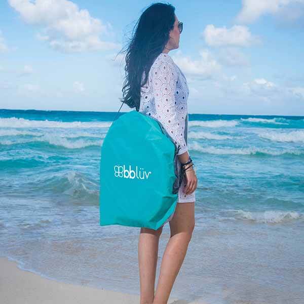Woman holding a teal bag with 'bbluv' branding on a beach.