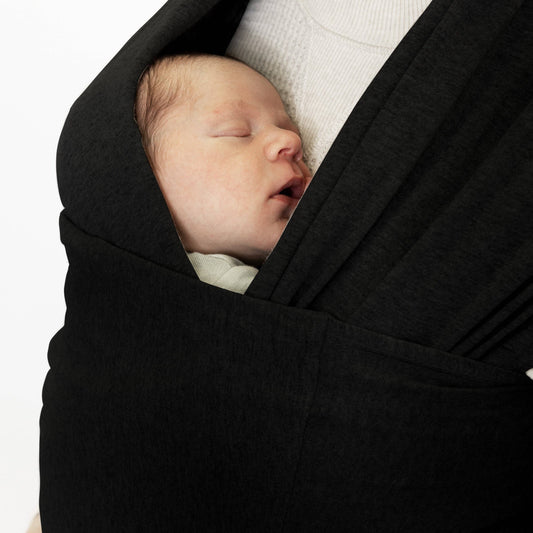 Newborn baby sleeping in a black wrap against a white background